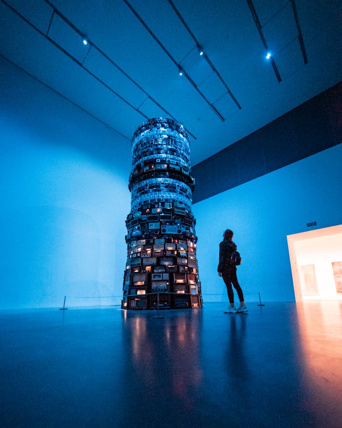 A woman observes a towering modern art installation under blue lighting in a gallery.