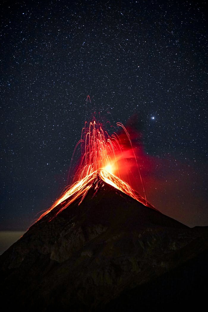 A breathtaking view of a volcano eruption with glowing lava against a starry night sky.