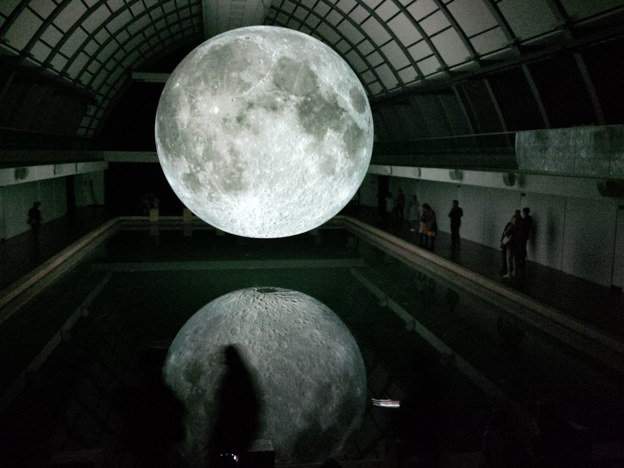 creative-02 Mesmerizing moon installation reflected in water indoors with people observing.