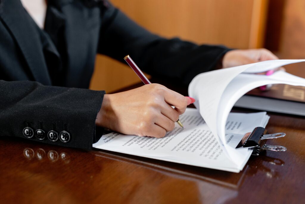 Terms Close-up of a woman signing legal documents with a pen in an office setting.